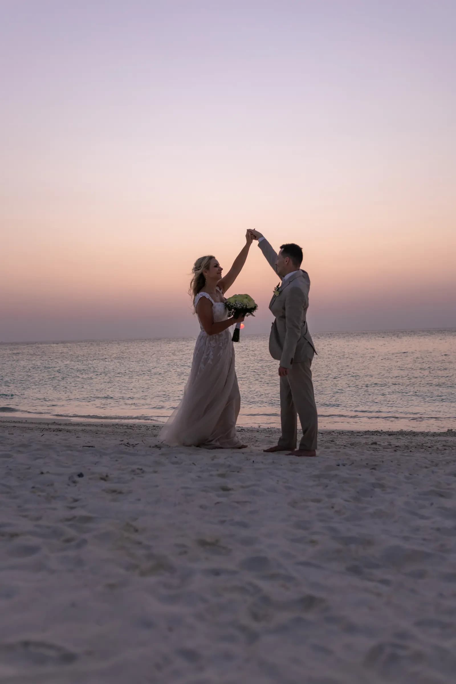 A couple dancing barefoot on the sand as the sun sets over the sea