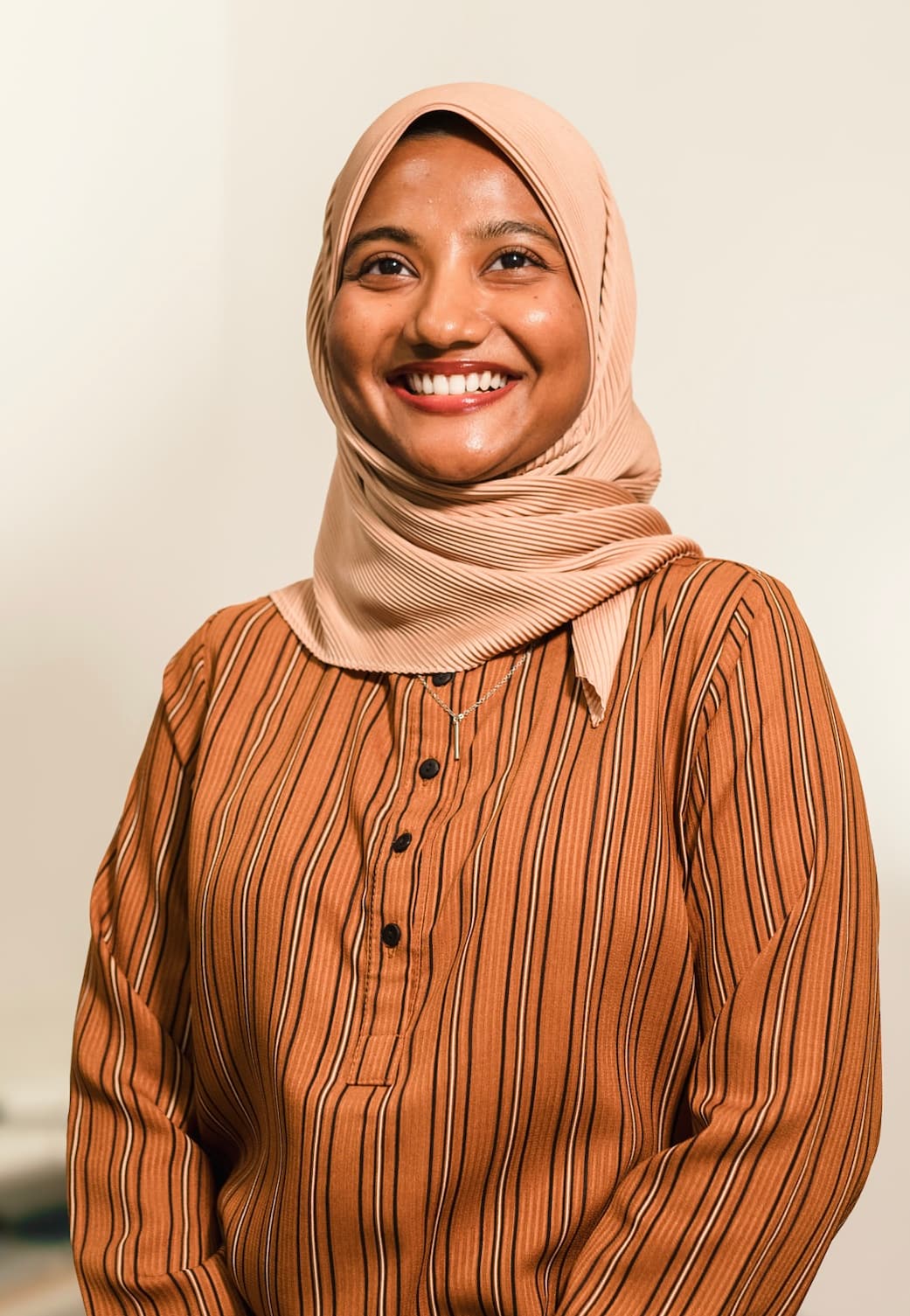 Aminath Shan, smiling, photographed against a plain light wall