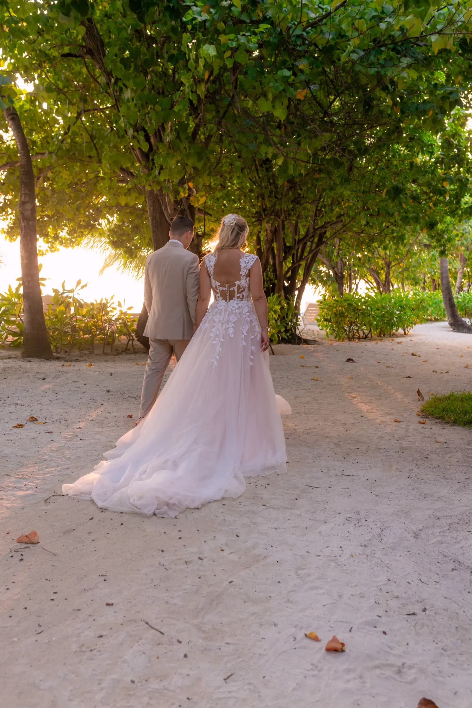 A couple walking hand in hand along a sandy path shaded by trees